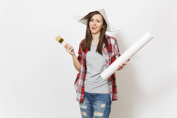 Irritated dissatisfied woman in casual clothes and newspaper hat holding wallpaper roll and paint brush isolated on white background. Instruments for renovation apartment room. Repair home concept. - Foto, immagini
