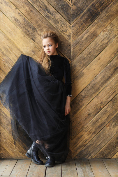 attractive little girl in black dress on the wooden background - Valokuva, kuva