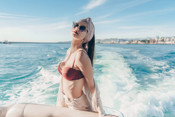 a luxurious young woman in a swimsuit and glasses travels, sails on a yacht on the blue sea - Foto, Imagen