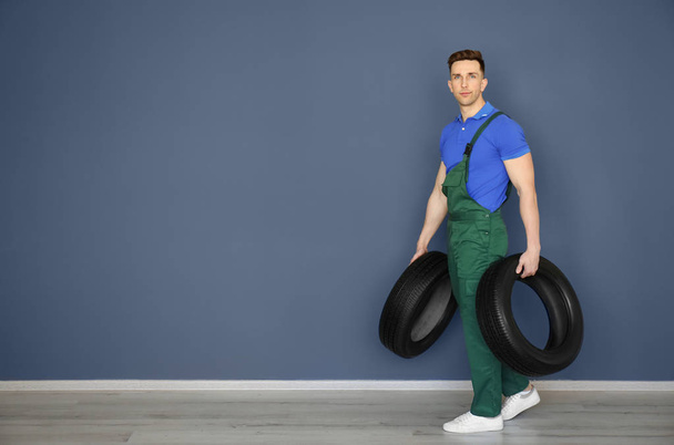 Male mechanic with car tires on grey wall background - Foto, Imagem