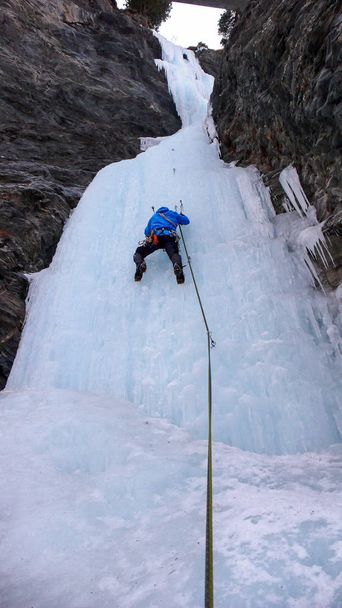 αρσενικό πάγο ορειβάτης σε ένα μπλε σακάκι ανεβαίνει παγωμένου καταρράκτη στην κοιλάδα του Avers στις Ελβετικές Άλπεις - Φωτογραφία, εικόνα