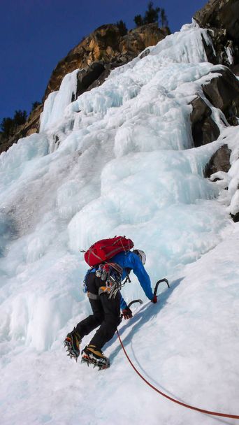 hombre escalador de hielo en una chaqueta azul en una cascada congelada gorgrous escalada en los Alpes en invierno profundo
 - Foto, Imagen
