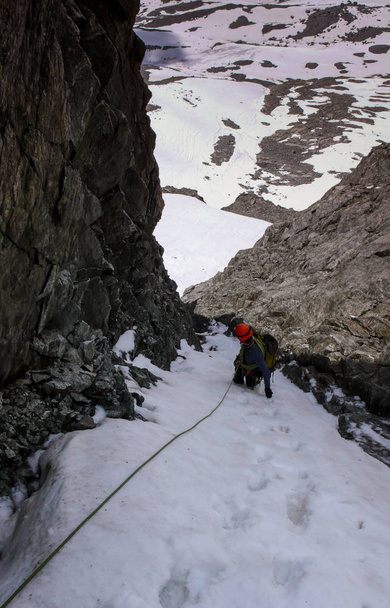 αρσενικό ορειβάτη σε ένα εξαιρετικά απόκρημνο και στενό λούκι σε ένα σχοινί και κοιτάζοντας προς τα κάτω - Φωτογραφία, εικόνα