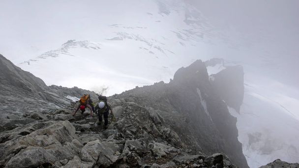 guide de montagne et client se dirigeant vers un sommet alpin élevé par une journée brumeuse
 - Photo, image