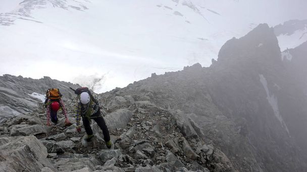 guía de montaña y cliente dirigiéndose hacia una cumbre alpina alta en un día de niebla
 - Foto, imagen