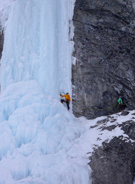 scalatore di ghiaccio maschio su una ripida cascata ghiacciata nelle Alpi vicino a Davos mentre il suo partner lo protegge da un punto sicuro
 - Foto, immagini