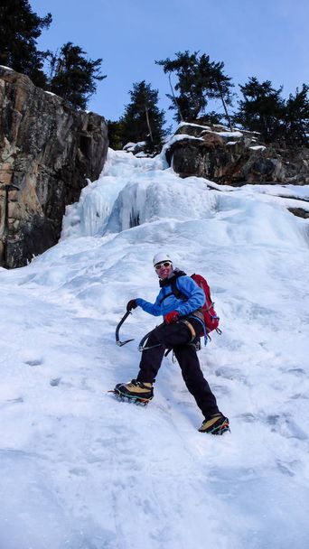 male ice climber in a blue jacket on a gorgeous frozen waterfall climbing in the Alps in deep winter - Photo, Image