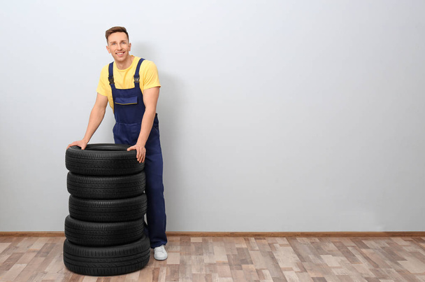 Male mechanic with car tires on light wall background - Valokuva, kuva