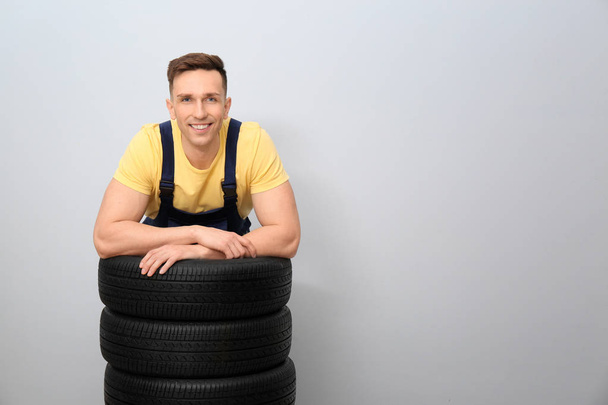 Male mechanic with car tires on light background - Foto, imagen