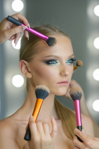 Woman getting powder on skin with makeup brushes. Woman with young face getting makeup in beauty salon - Foto, Imagem