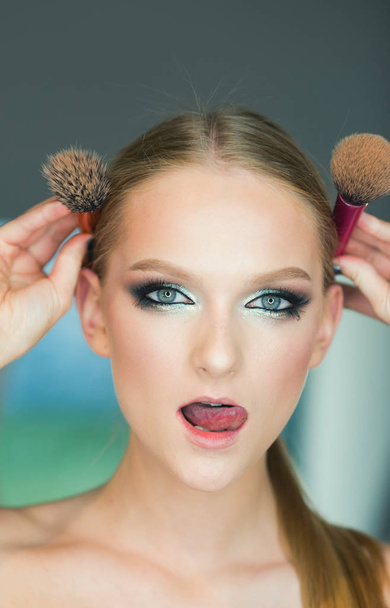 Girl with young skin face, skincare, youth. Woman with makeup face hold brushes at head. Woman with blond hair and makeup brushes, beauty. Beauty model with glamour look, hairstyle - Photo, Image