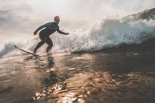 Joven surfeando una ola al atardecer
 - Foto, imagen