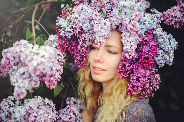 Buiten mode foto van een mooie jonge vrouw die blauwogige. Lente kleur. mooie blonde meisje in lila bloemen. Parfum met een geur van bloemen. Parfums en schoonheid - Foto, afbeelding