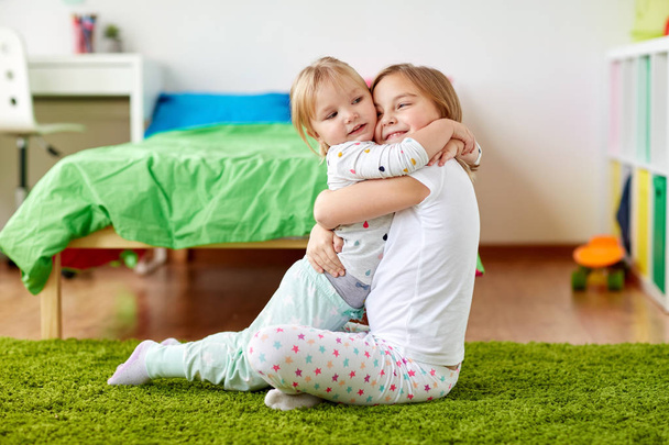 happy little girls or sisters hugging at home - Foto, afbeelding