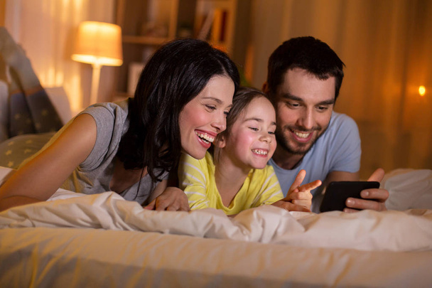 happy family with smartphone in bed at night - Фото, изображение