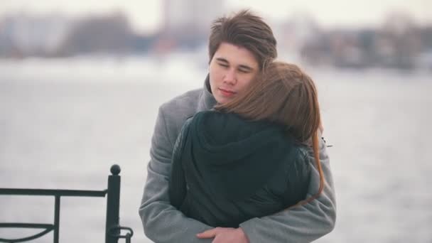 Молодой человек обнимает свою девушку на заднем плане на берегу реки
 - Кадры, видео