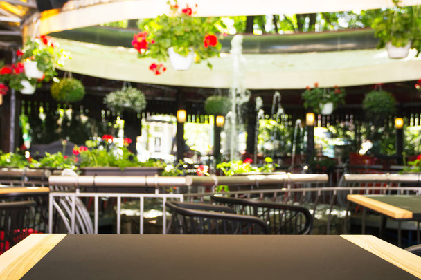 Empty table in front of a blurred background. A light street cafe with flowers, plants and a fountain - can be used to display or install your products. A layout for displaying the product. - Photo, Image