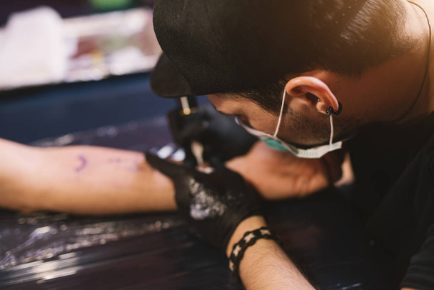 young focused tattoo artist inking arm of customer - Photo, Image
