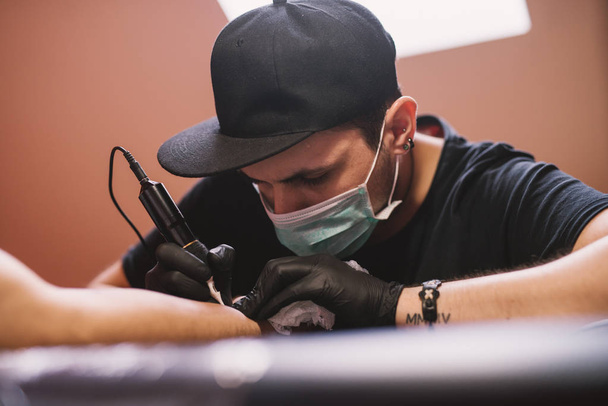 młody koncentruje się artysta tatuażu odbarwiania ramienia klienta - Zdjęcie, obraz