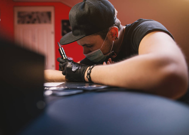νέοι επικεντρώθηκε καλλιτέχνης τατουάζ μελανιού βραχίονα του πελάτη - Φωτογραφία, εικόνα