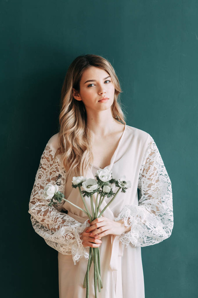Young beautiful bride in boudoir and wedding dress, with a wreath and a bouquet in her hands. London wedding trends, stylish photoshoot - Fotó, kép