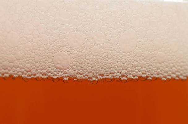 Φυσαλίδες από ένα κοντινό πλάνο αφρό μπύρα σε μισό ποτήρι. - Φωτογραφία, εικόνα