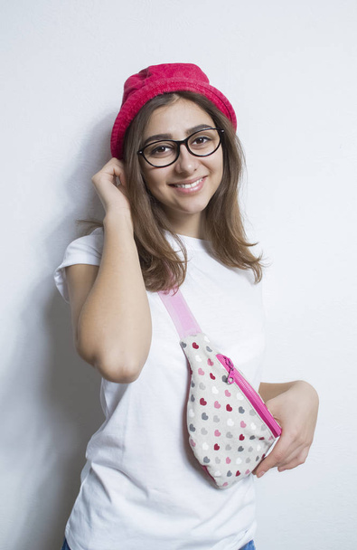 Πορτραίτο του happy εφηβικό κορίτσι με τα γυαλιά σε λευκό φόντο. Νεαρή Τουρκάλα χαμογελώντας. Γελώντας Καυκάσιος φοιτήτριας κατέχει τσαντάκι μέσης μπανάνα - Φωτογραφία, εικόνα