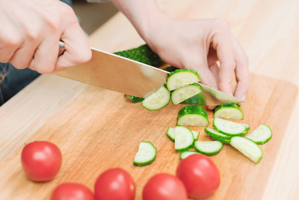 close-up of female hands cut into fresh cut cucumbers on a wooden cutting board next to pink tomatoes. The concept of homemade vegetarian cuisine and healthy eating and lifestyle - Zdjęcie, obraz