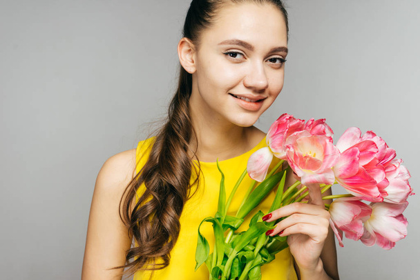 happy young girl in yellow dress holds a bouquet of fragrant flowers in hands and smiles - Фото, зображення