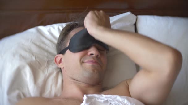 Young man in a mask for sleeping, sleeping in bed on a pillow in the daytime. 4k. - Filmagem, Vídeo