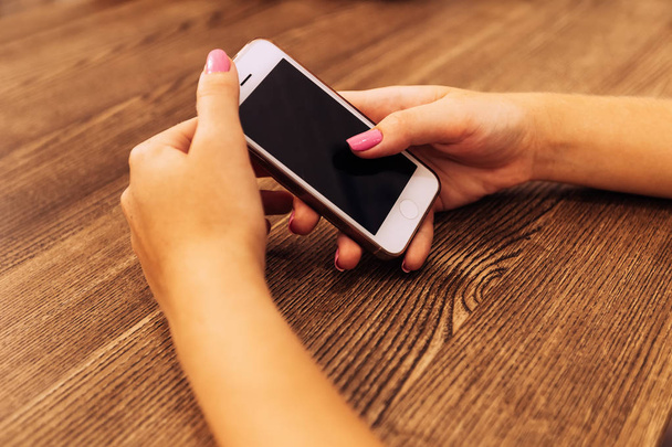 μοντέρνο λευκό τηλέφωνο στα χέρια του κοριτσιού που κάθεται στο τραπέζι - Φωτογραφία, εικόνα