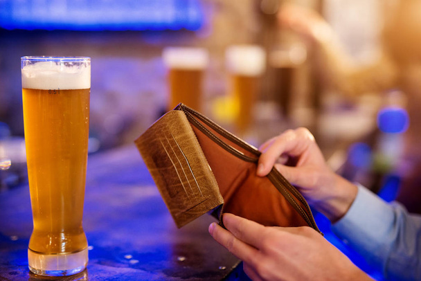 mãos masculinas segurando carteira vazia com cerveja na mesa no bar
 - Foto, Imagem
