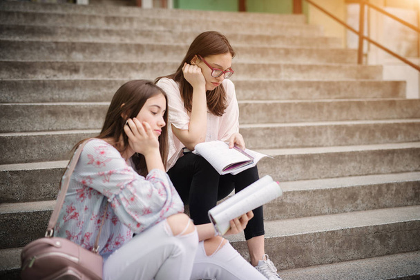 2 つの悲しいきれいな女子高校生階段で一緒にノートを読んで  - 写真・画像