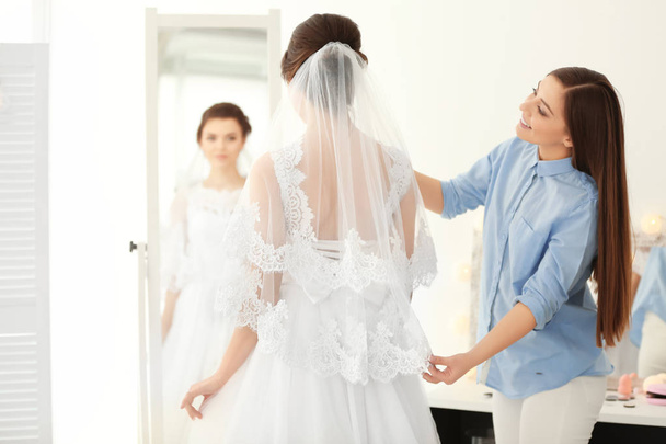Fashion stylist preparing bride before her wedding in room - Фото, изображение