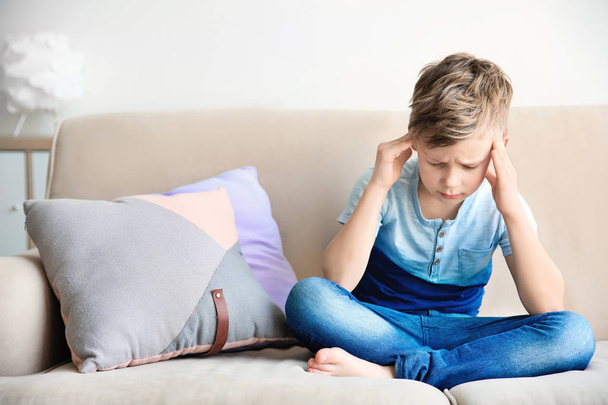 Little boy suffering from headache while sitting on couch at home - Foto, Bild