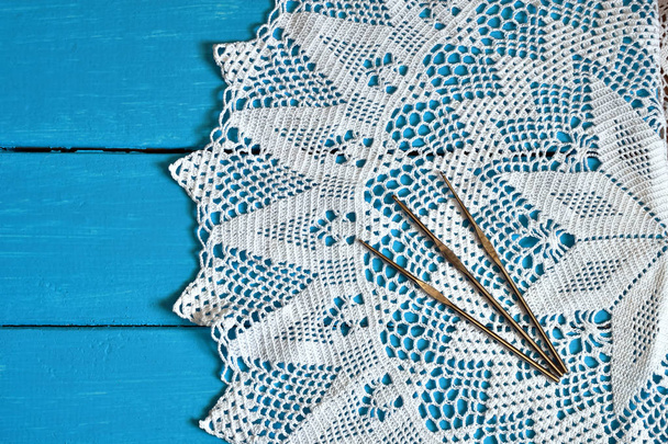 Uma imagem de vista superior de um laço branco crochê guardanapo e três ganchos de crochê de metal em um fundo azul brilhante
. - Foto, Imagem