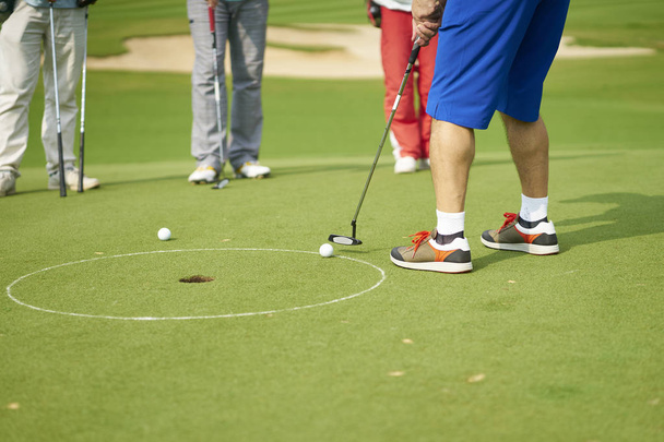 Unbekannter Asiate legt Golfball im Sommer auf Grün - Foto, Bild