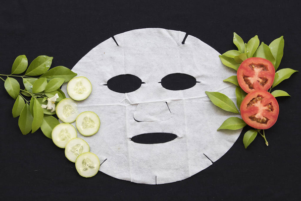 természetes lap maszk egészségügyi kivilágosodott bőr arc a paradicsom és az uborka, a háttér fekete - Fotó, kép