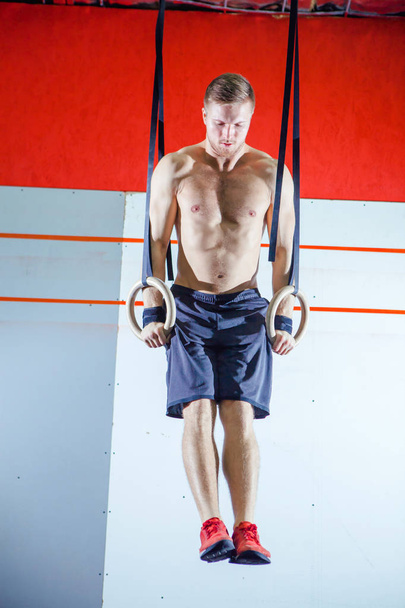Muscle-up exercise young man doing intense cross fit workout at the gym on gymnastic rings. - Foto, afbeelding
