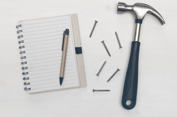 Construction concept background with copy space. Blank note pad with empty paper sheet, pen and hammer with nails on the table. Construction tricks. - Photo, image