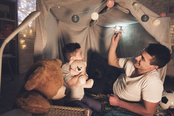 Father and son playing with toy airplane and cars in blanket fort  - Foto, immagini