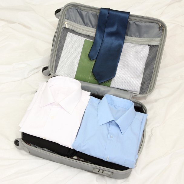 Open grey suitcase with clothing on bed - Fotografie, Obrázek