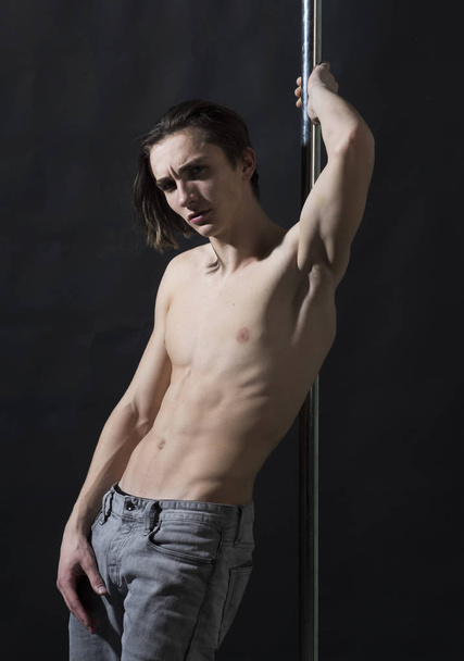 Macho with naked chest, athlete, sportsman, dancer performing pole dancing moves. Sexy dancer concept. Sexy, attractive guy lean on metallic pole. Man on pensive face with nude torso, black background - Фото, зображення