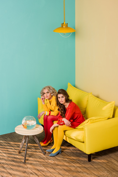 mulheres retro estilo sentado no sofá amarelo com peixes de aquário na mesa de café no apartamento colorido, conceito de casa de boneca
 - Foto, Imagem