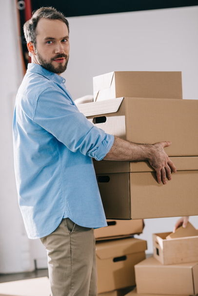 бородатый бизнесмен держит картонные коробки и смотрит в камеру во время переезда в новый офис
 - Фото, изображение
