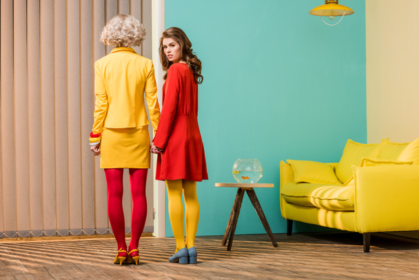 カラフルなアパート、人形の家のコンセプトで手を繋いでいる明るい色のレトロなスタイルの服の女性の背面図 - 写真・画像