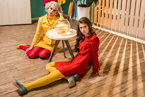 young retro styled women sitting on floor near golden fish in aquarium on coffee table, doll house concept - Photo, Image