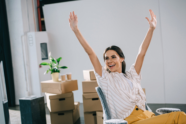 excited young businesswoman raising hands and looking away in new office - Photo, Image