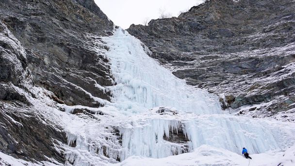mannelijke ice climber staat op de headwall van een lange en steile waterval in de Alpen - Foto, afbeelding