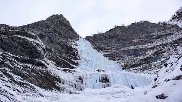 escalador de gelo macho fica na parede de uma longa e íngreme cachoeira nos Alpes
 - Foto, Imagem